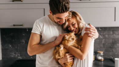 brunette man looking at his cat and embracing wife indoor portrait of happy family posing with pet scaled 1 1